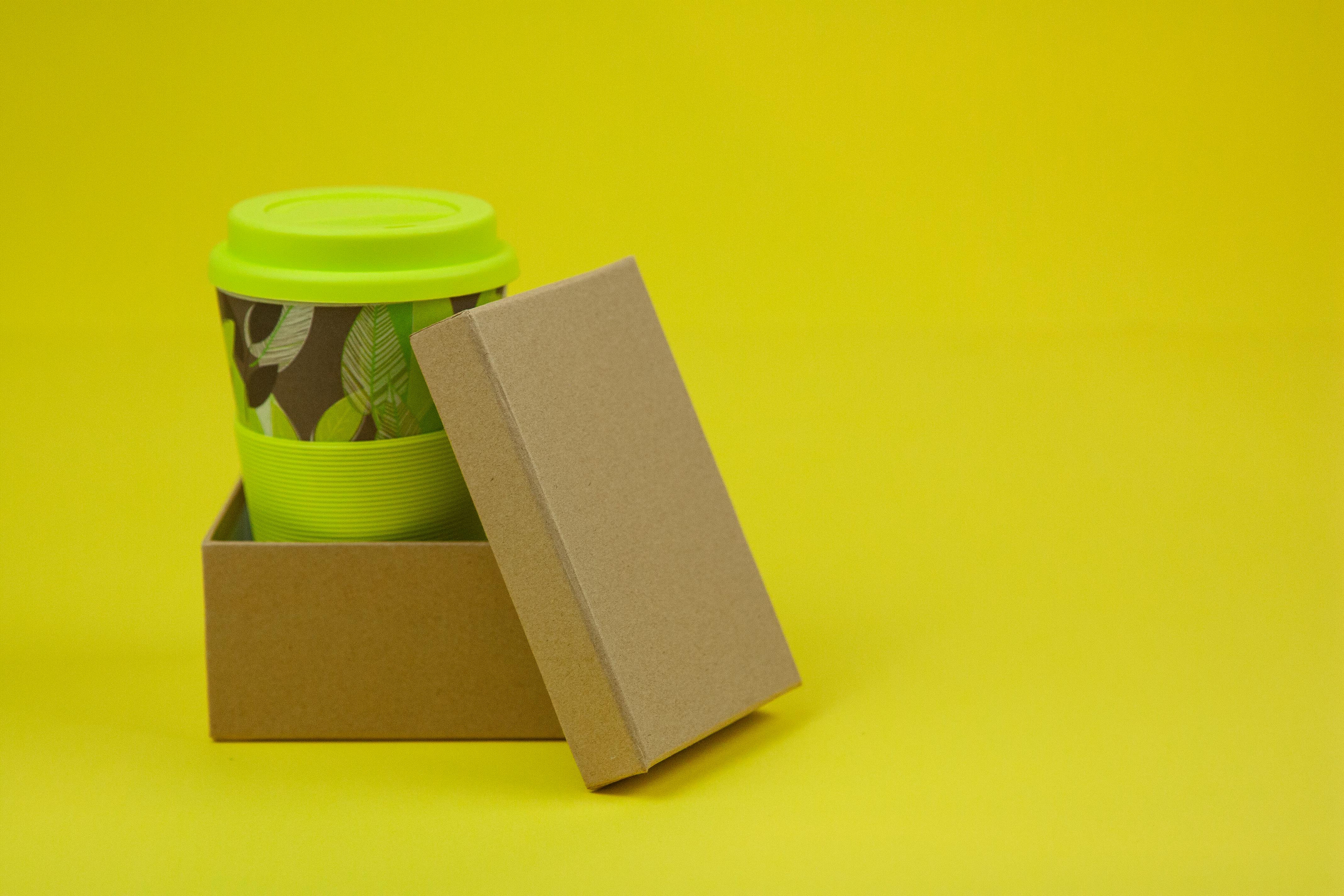 Green coffee cup inside cardboard box with a yellow background