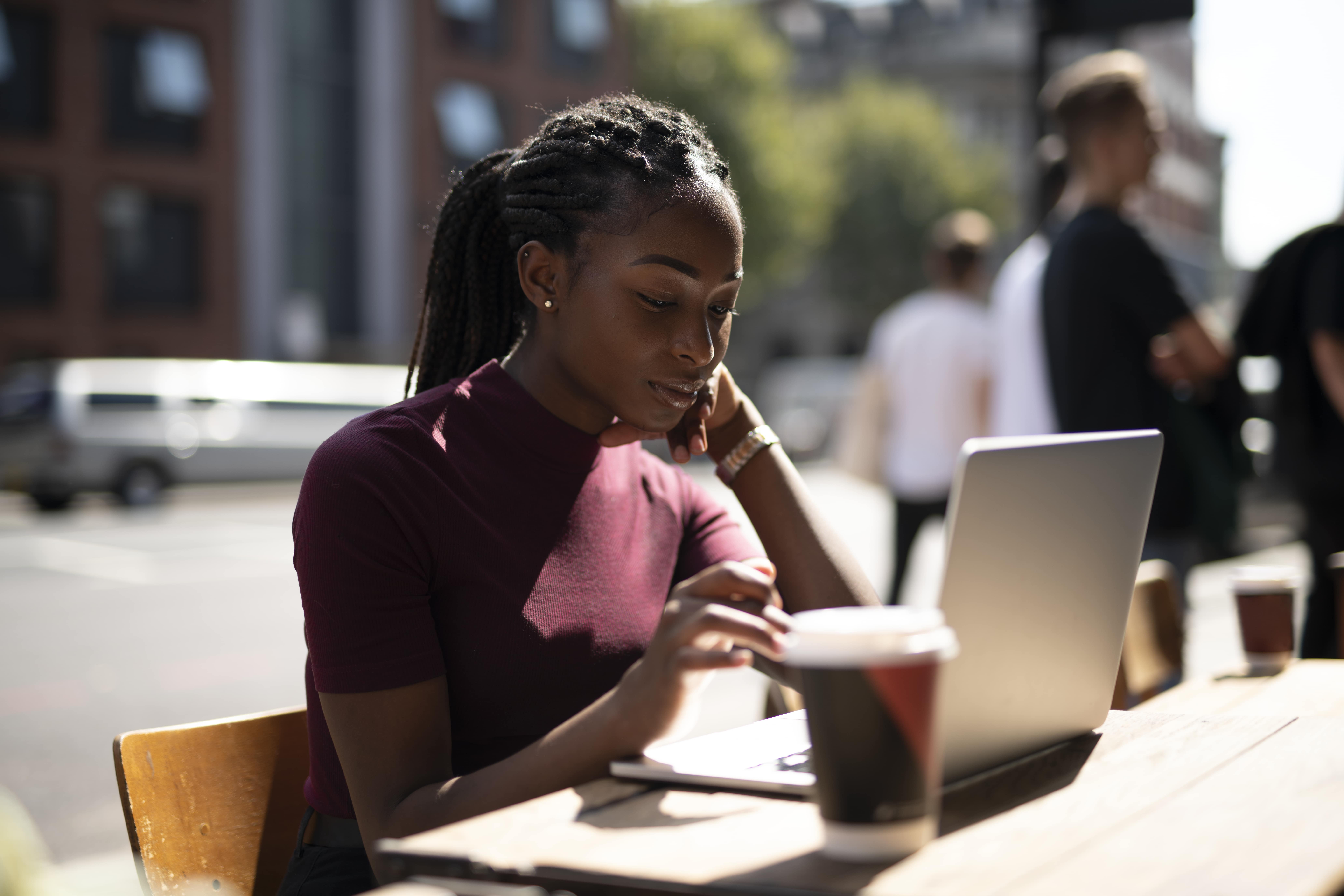 Woman working on her laptop from a cafe, with a cup of coffee