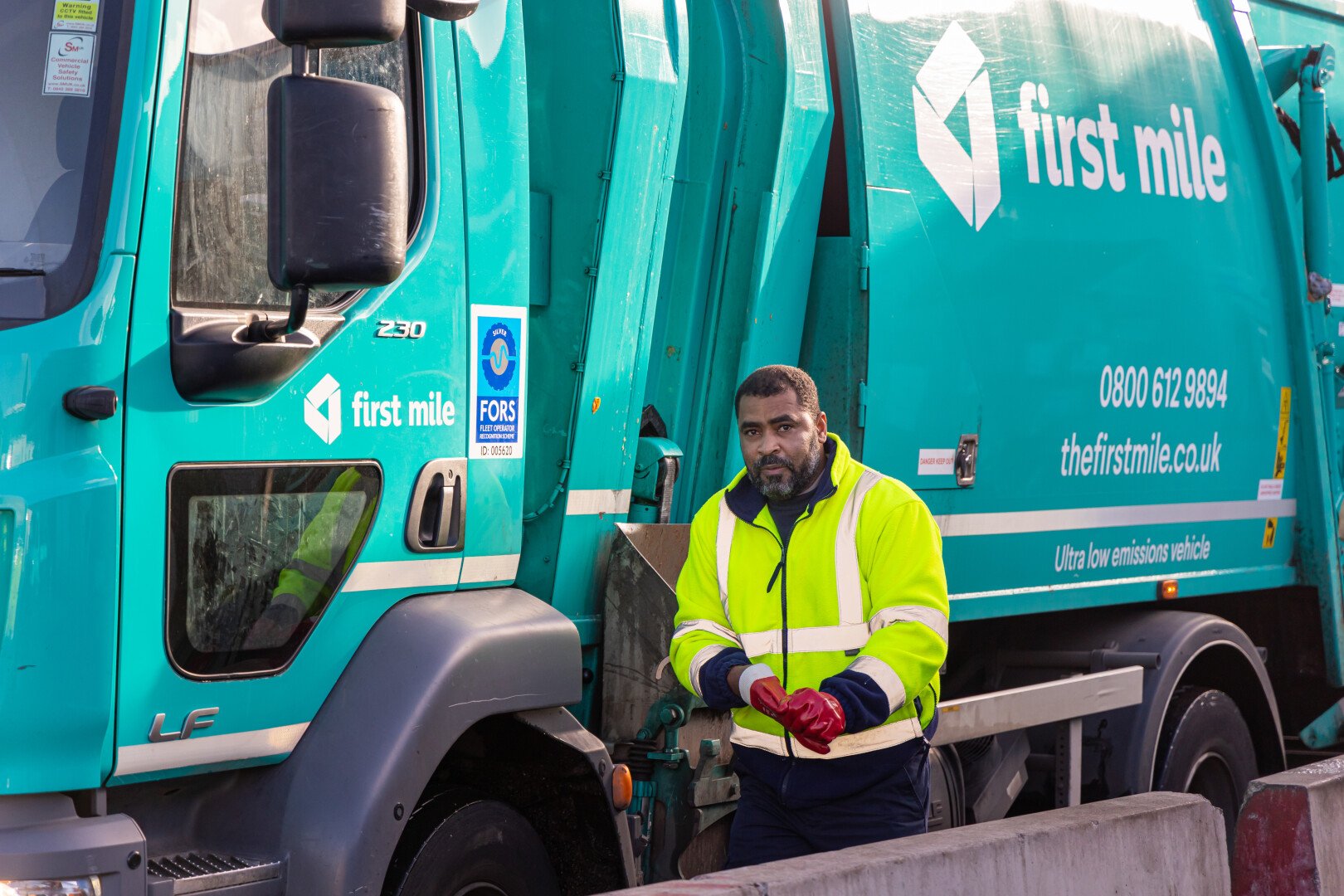 A First Mile worker besides a waste compactor van
