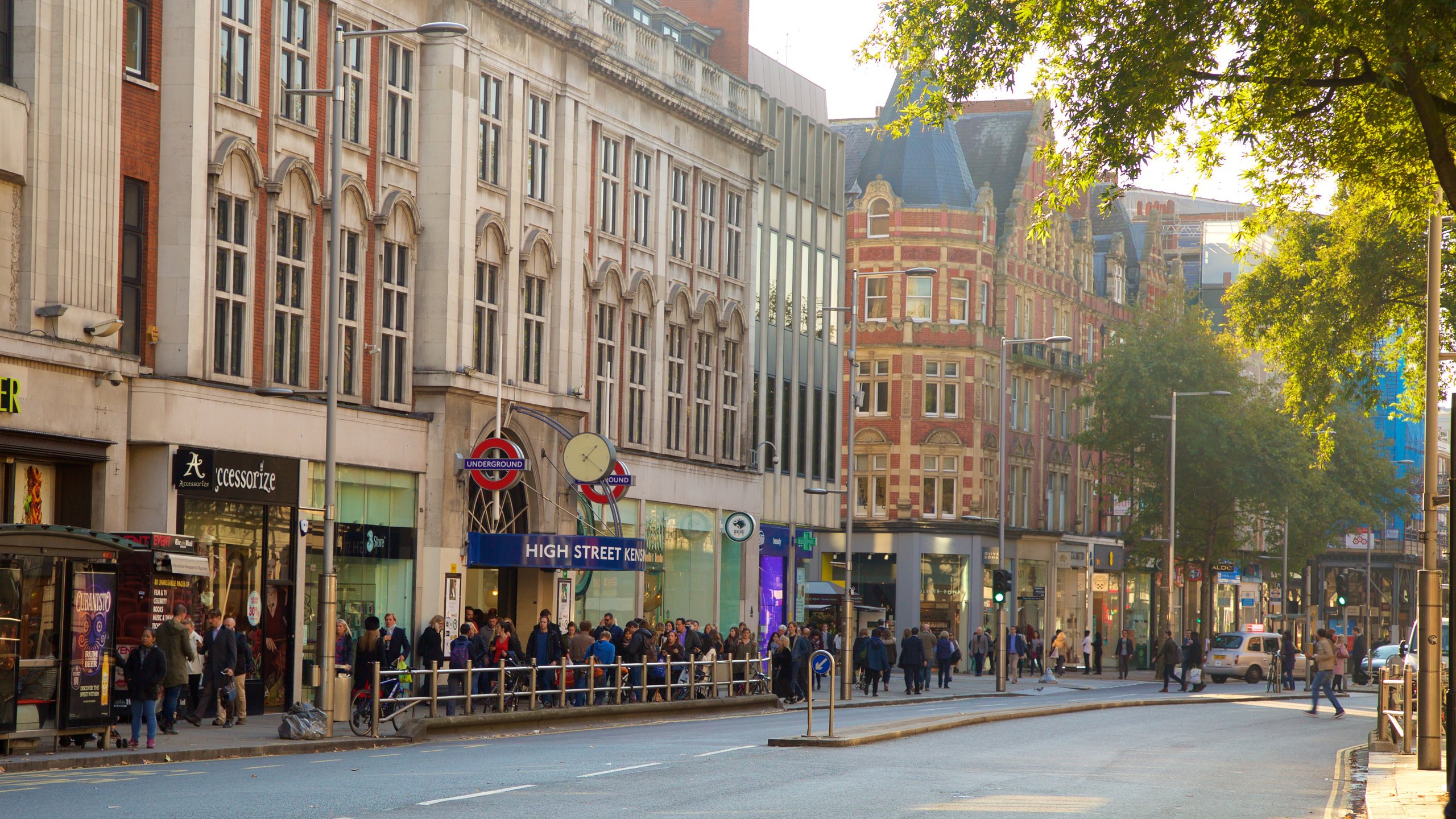View of Kensington High Street Underground Station in London with shoppers and storefronts