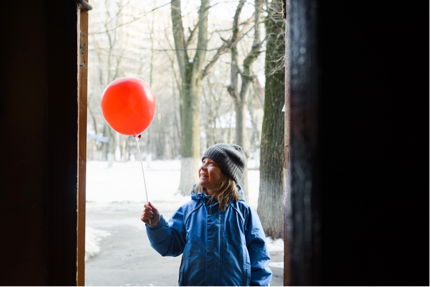 Child holding a red balloon, smiling outdoors