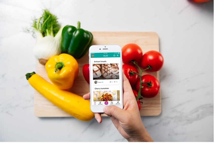 A mobile phone showing the OLIO app in front of fruit and veg placed on a chopping board