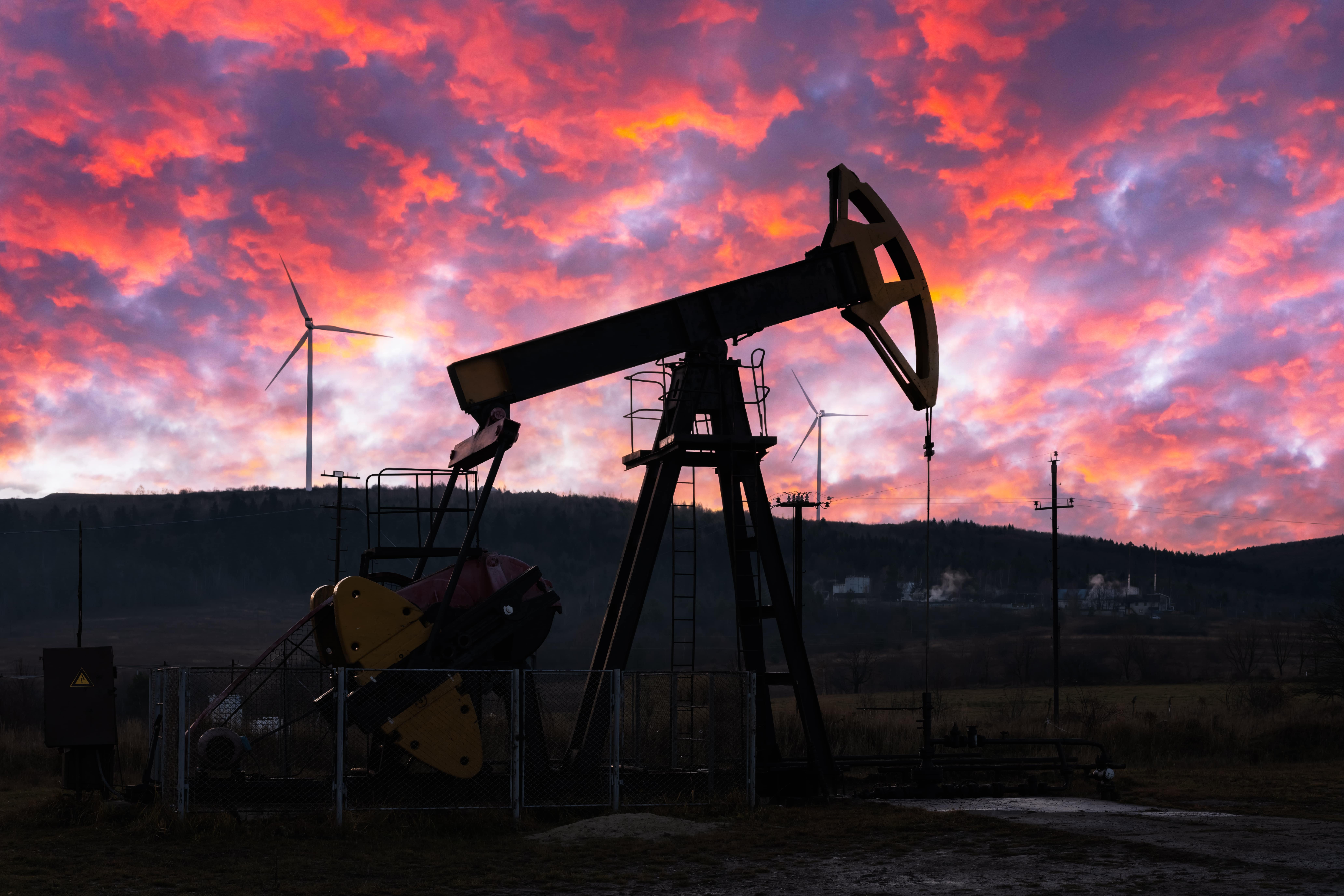 Oil pump and wind turbines contrasting against a purple sky, symbolizing energy transition